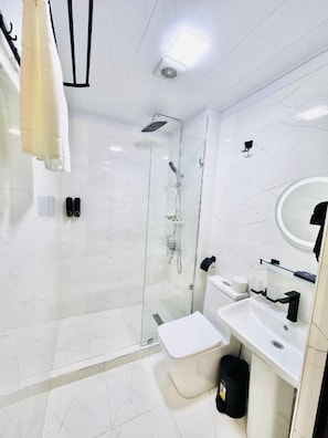 A modern bathroom with a glass-enclosed shower, a white toilet, and a sink with a mirror. - The Moonya Hotel (Samarqand)