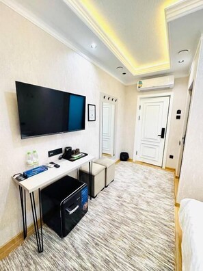 Ein Hotelzimmer mit Flachbildfernseher, Schreibtisch mit Stuhl, Bett, Teppichboden und einer Tür.