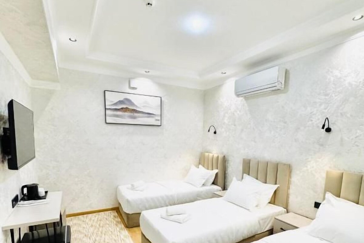 A hotel room with two beds, a desk, a chair, a television, and a wall-mounted air conditioner.