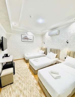 A hotel room with two beds, a desk, a chair, a television, and a wall-mounted air conditioner. - The Moonya Hotel (Samarqand)