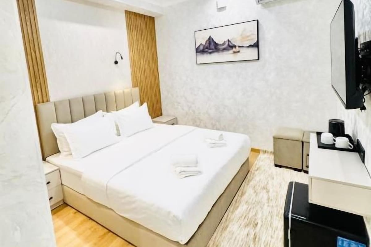 A modern hotel room with a large bed, a desk with a computer, and a mounted TV.