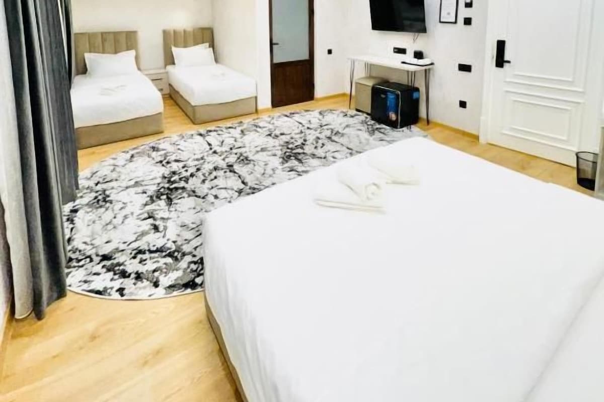 A modern hotel room with a large bed, a desk, a television, and a wardrobe.