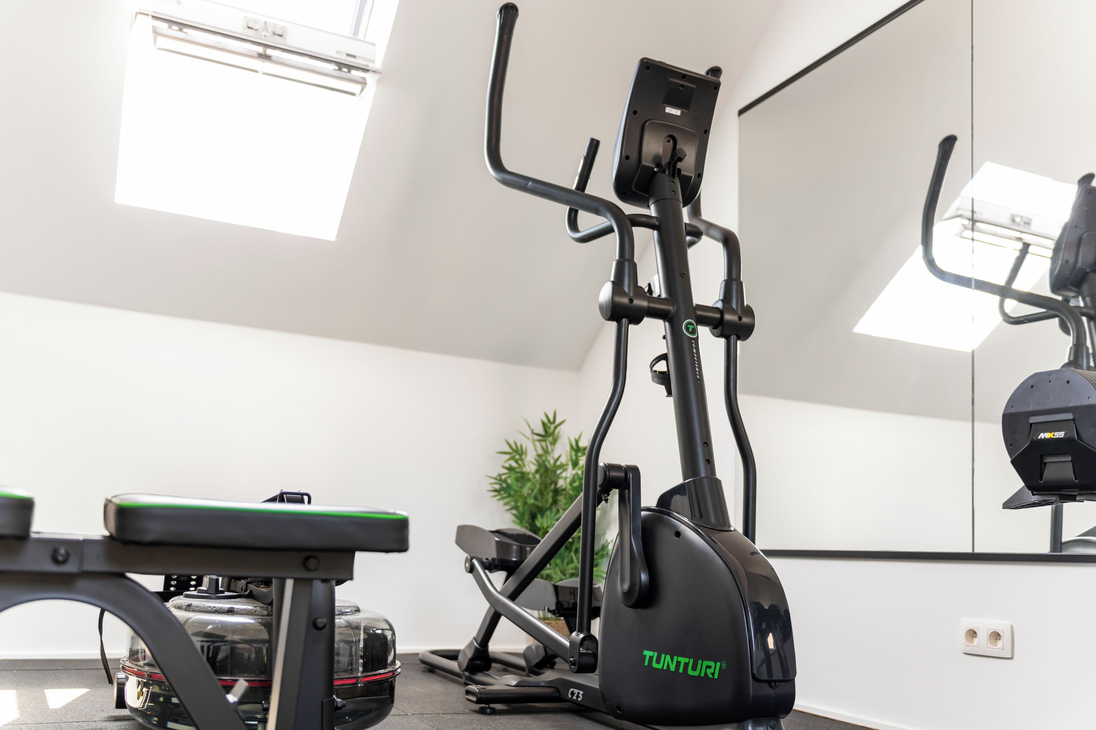 Une salle de sport équipée de matériel d’exercice, d’un banc et d’un appareil elliptique de la marque Tunturi.