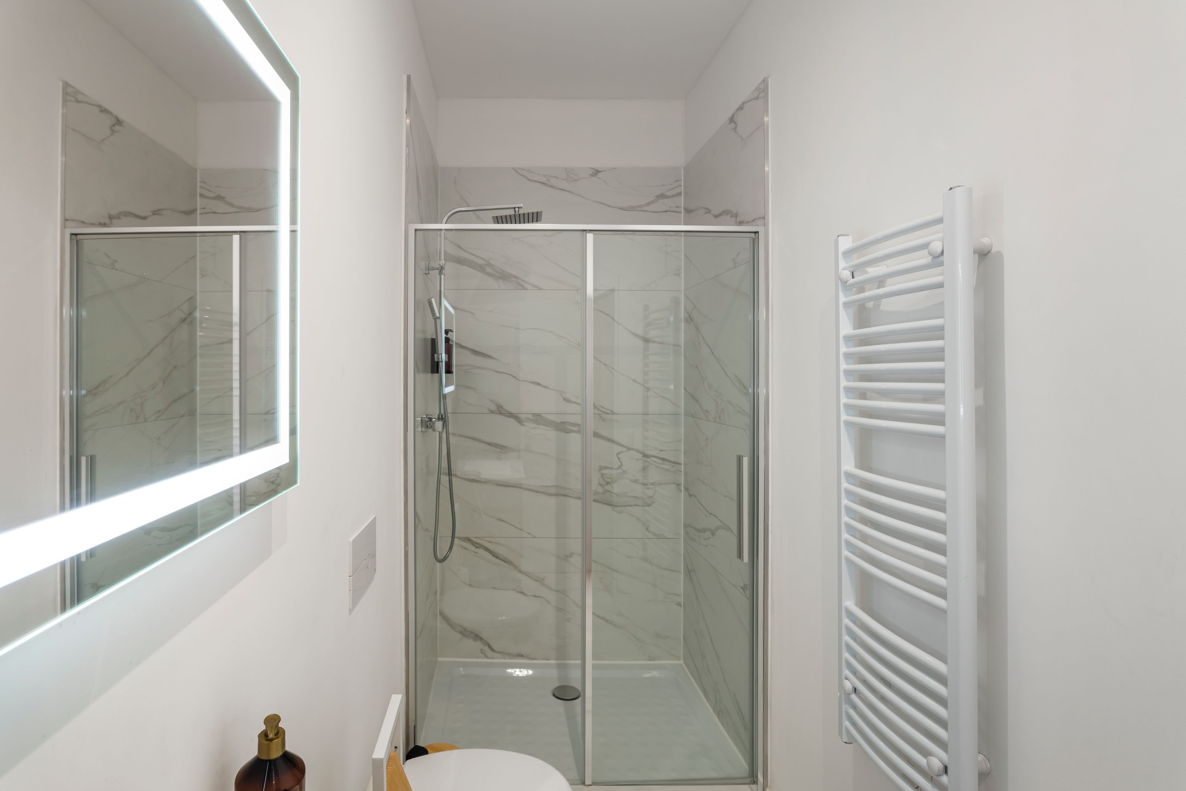 A modern bathroom with a glass-enclosed shower, a white toilet, and a large mirror.