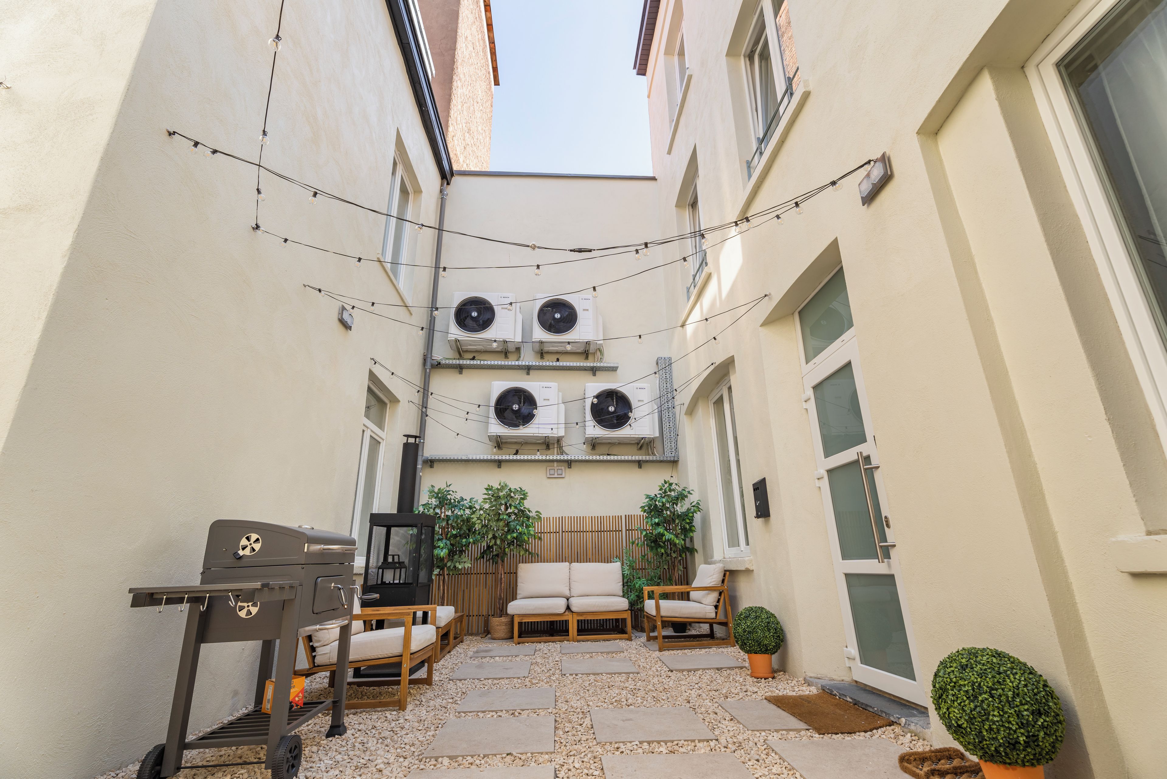 A narrow outdoor space with a grill, seating, and potted plants.