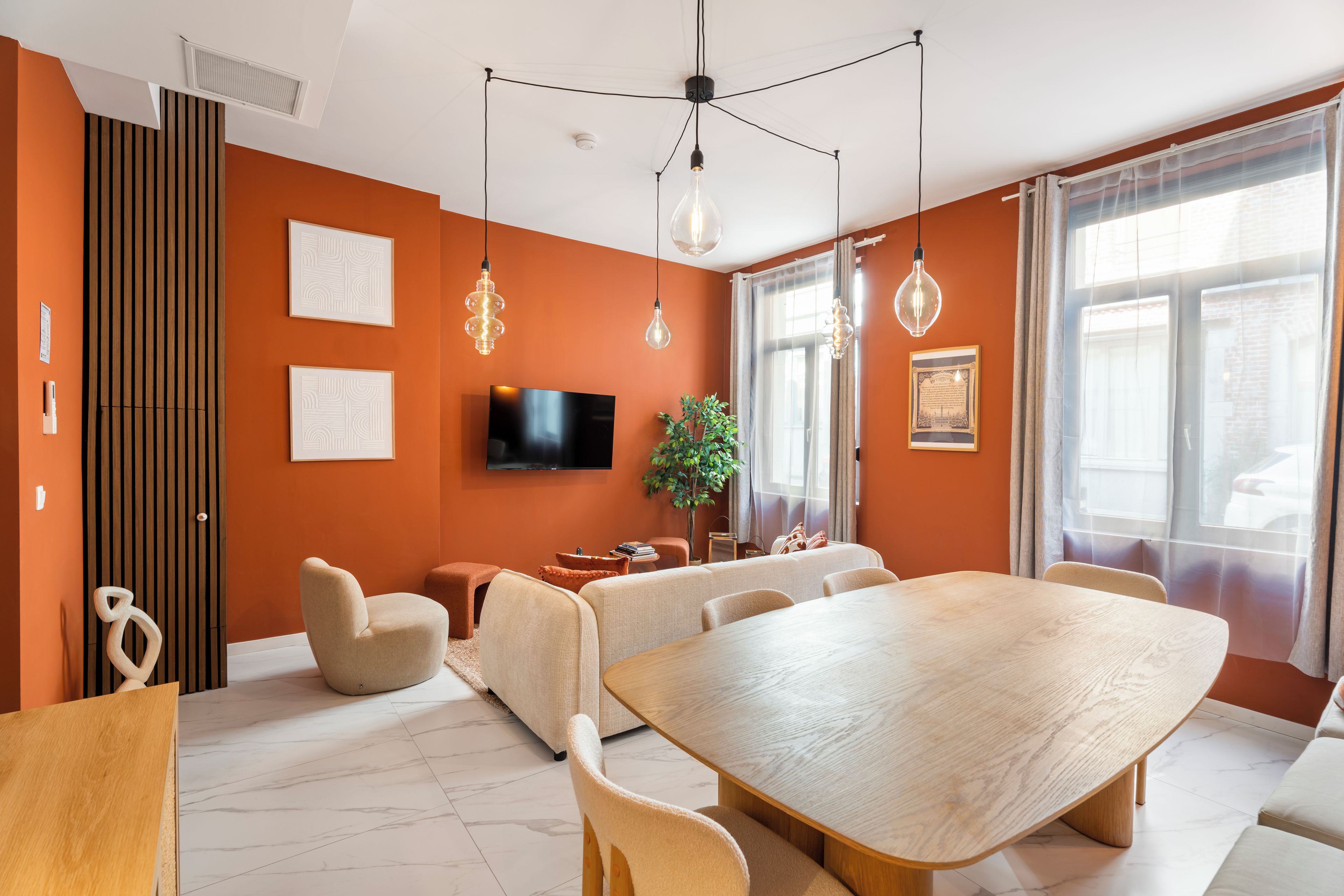 Un salon moderne avec une grande table à manger en bois, des sièges confortables, un téléviseur à écran plat et une grande fenêtre agrémentée de rideaux.