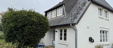 Una casa blanca con techo gris, pared de piedra y una silla azul en el jardín.