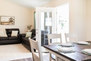 Un coin repas avec une table dressée pour quatre personnes, des chaises et une vue sur un salon comprenant un canapé et un tableau.