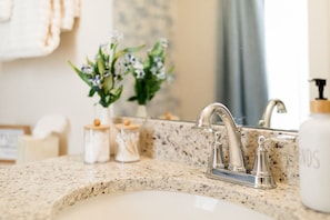 Une salle de bain avec un comptoir en granit, un robinet argenté et un flacon de savon pour les mains.
