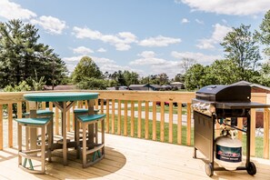 Une terrasse en bois équipée d’un barbecue et d’une bouteille de propane, entourée d’une clôture en bois et de verdure.