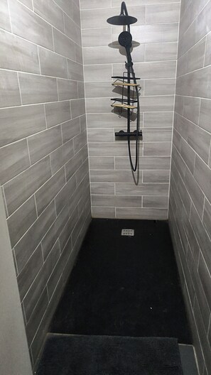 A shower area with grey tiles, a black showerhead, and a black mat.
