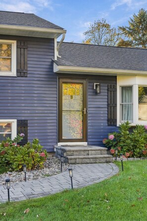 A two-story house with a dark blue siding exterior, a front door with a glass panel, and a small porch with steps.