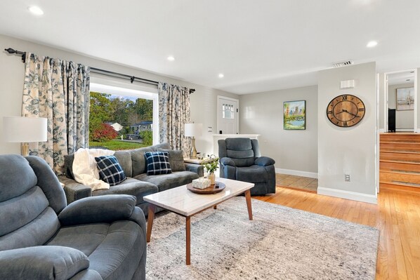 A modern living room with a sofa, armchairs, a coffee table, and a large window with curtains.