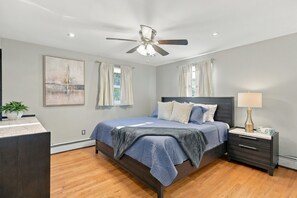 A bedroom with a bed, nightstand, lamp, ceiling fan, and artwork on the wall.