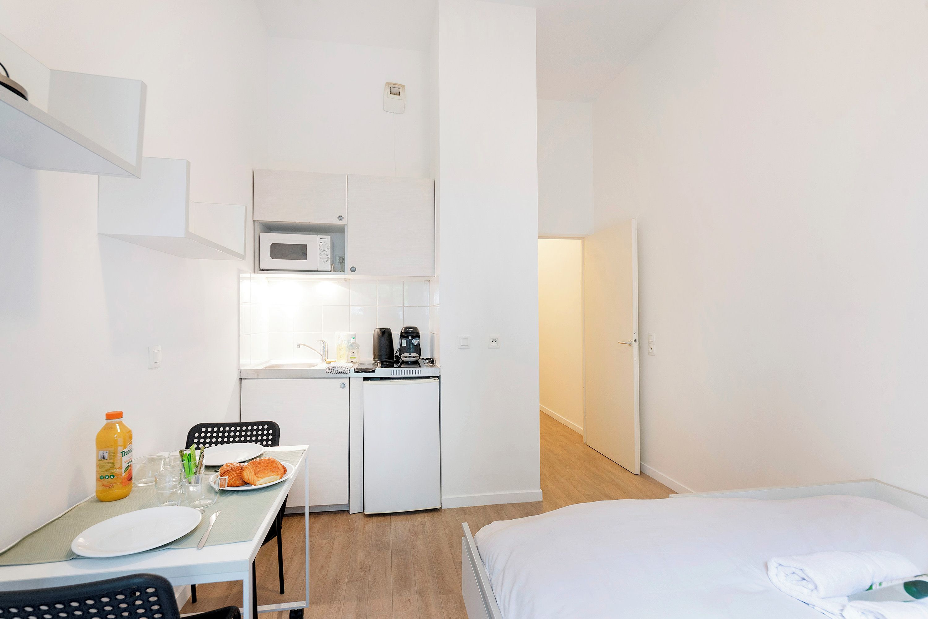 Quarto de hotel compacto com cozinha compacta, área de refeições e uma cama.