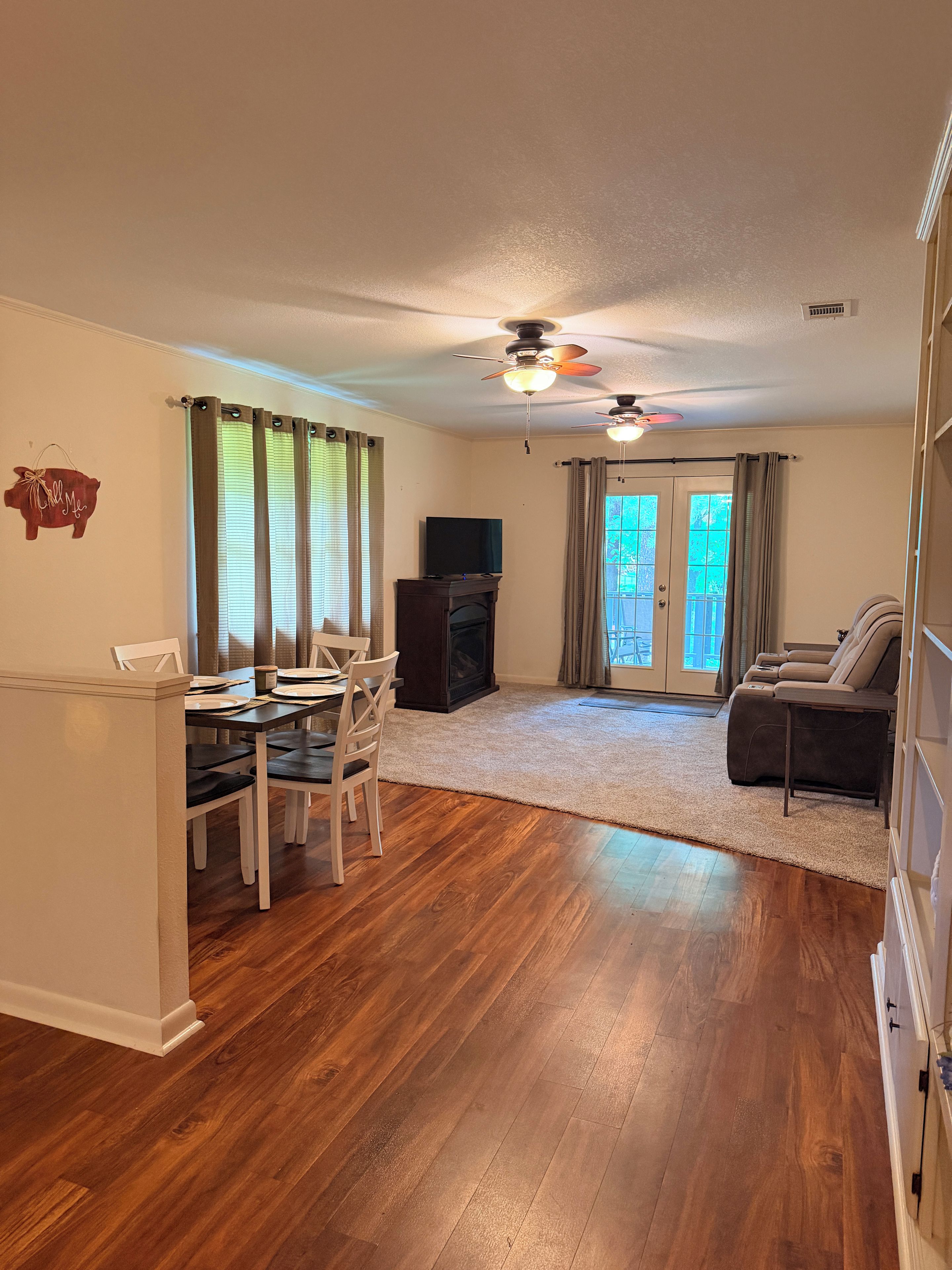 A living room with a dining area, wooden flooring, a ceiling fan, and a television.