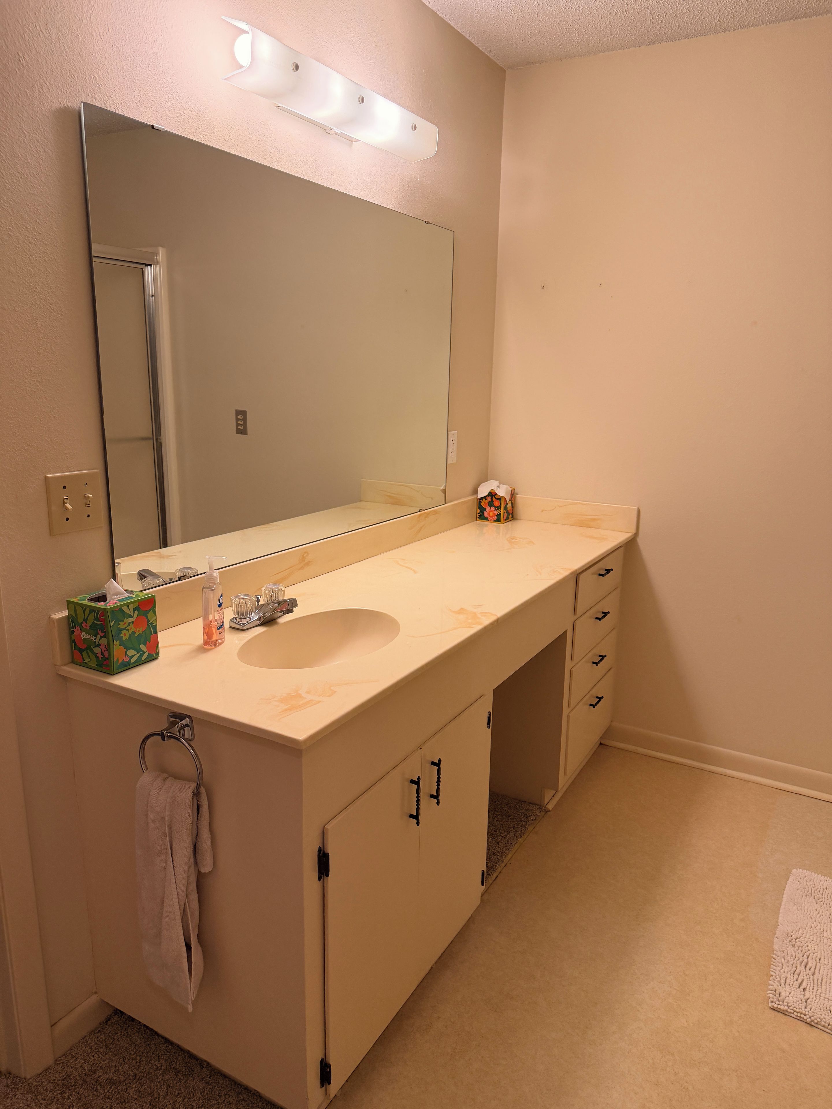 A bathroom with a large mirror, a sink, and a vanity with drawers.