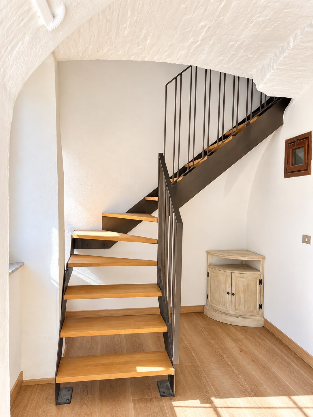 A staircase with wooden steps and a metal railing, leading to a landing with a wooden cabinet.