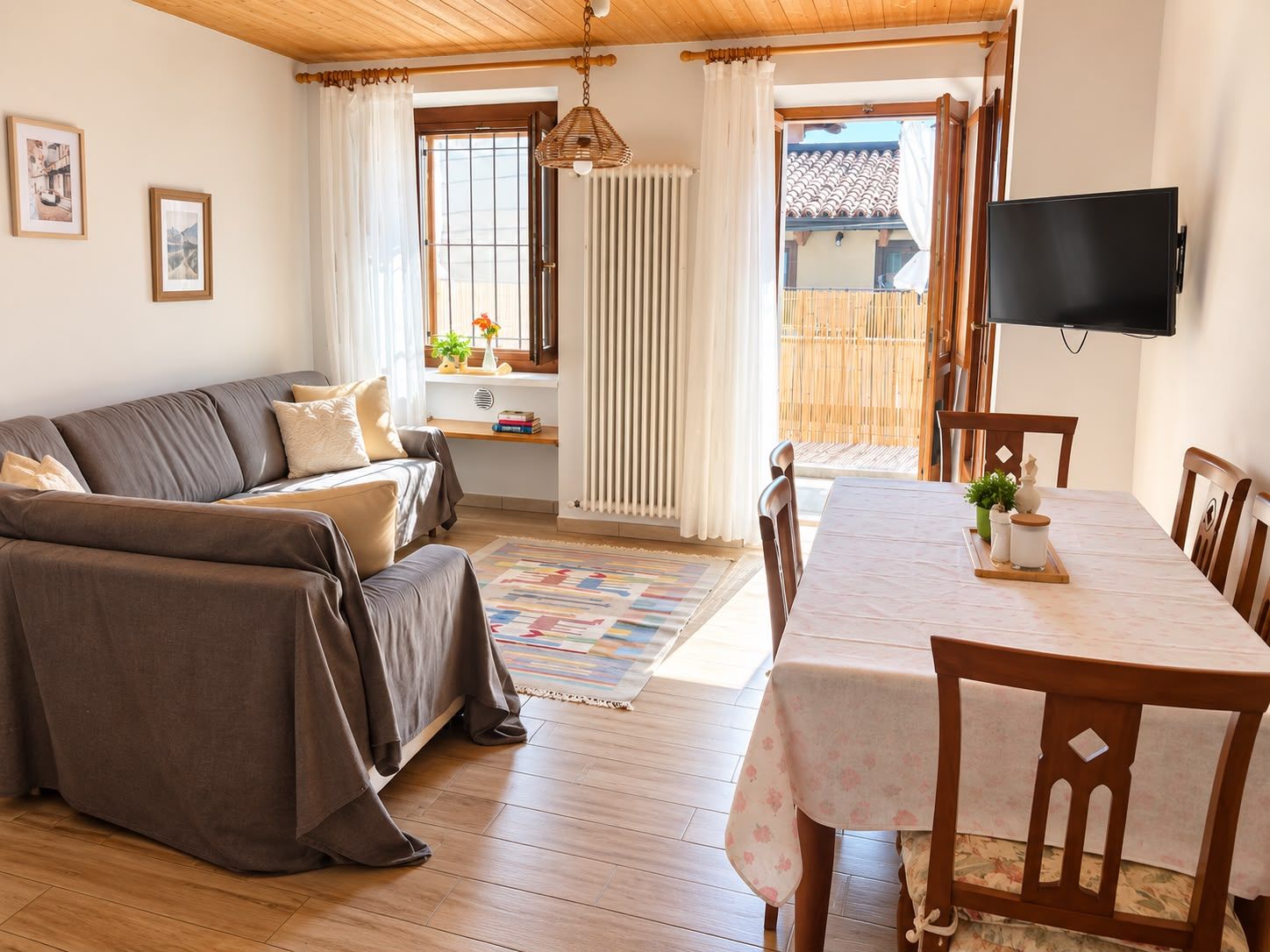 Una sala de estar acogedora con un sofá, una mesa de comedor con sillas, un televisor y una ventana con cortinas.