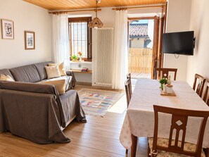 A cozy living room with a sofa, a dining table with chairs, a TV, and a window with curtains.