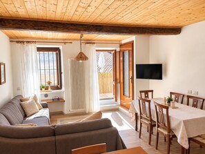 A cozy living room with a sofa, a dining table with chairs, a TV mounted on the wall, and a window with curtains.