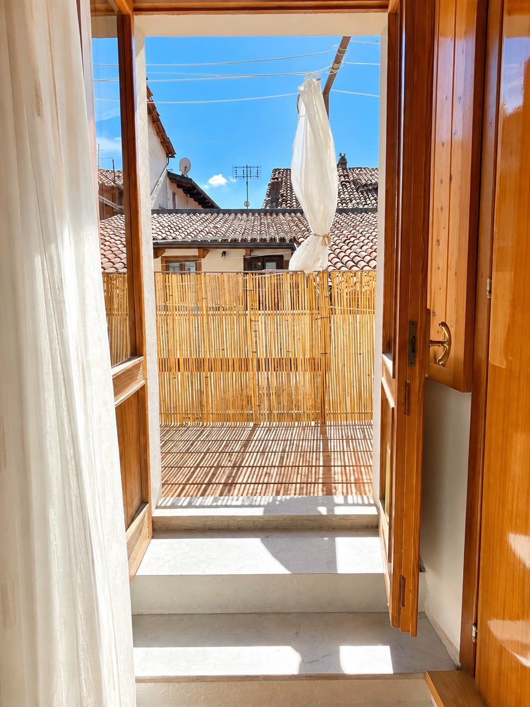 A wooden door leading to a balcony with a bamboo fence and a tiled roof in the background.