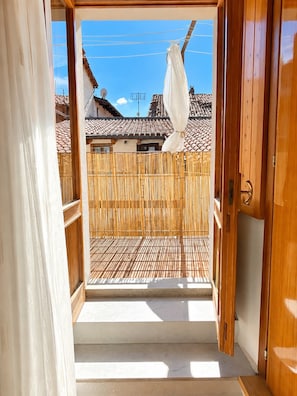 En trædør der fører ud til en balkon med et bambushegn og et tag med fliser i baggrunden.