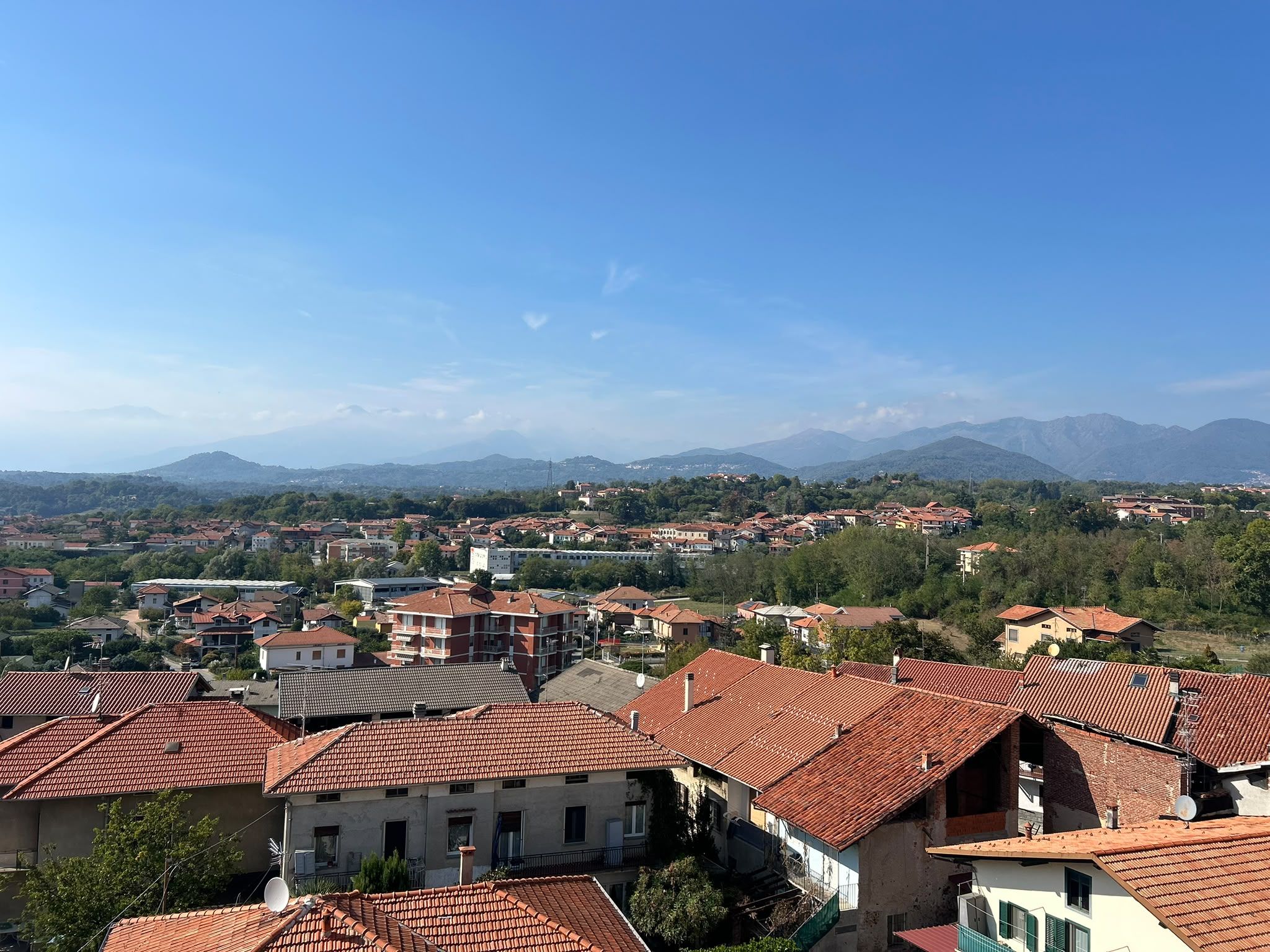 Ein Wohngebiet mit roten Ziegeldächern, umgeben von viel Grün und Bergen im Hintergrund.
