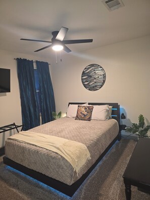 Une chambre à coucher comprenant un lit, un ventilateur de plafond, un téléviseur fixé au mur et un élément décoratif mural.