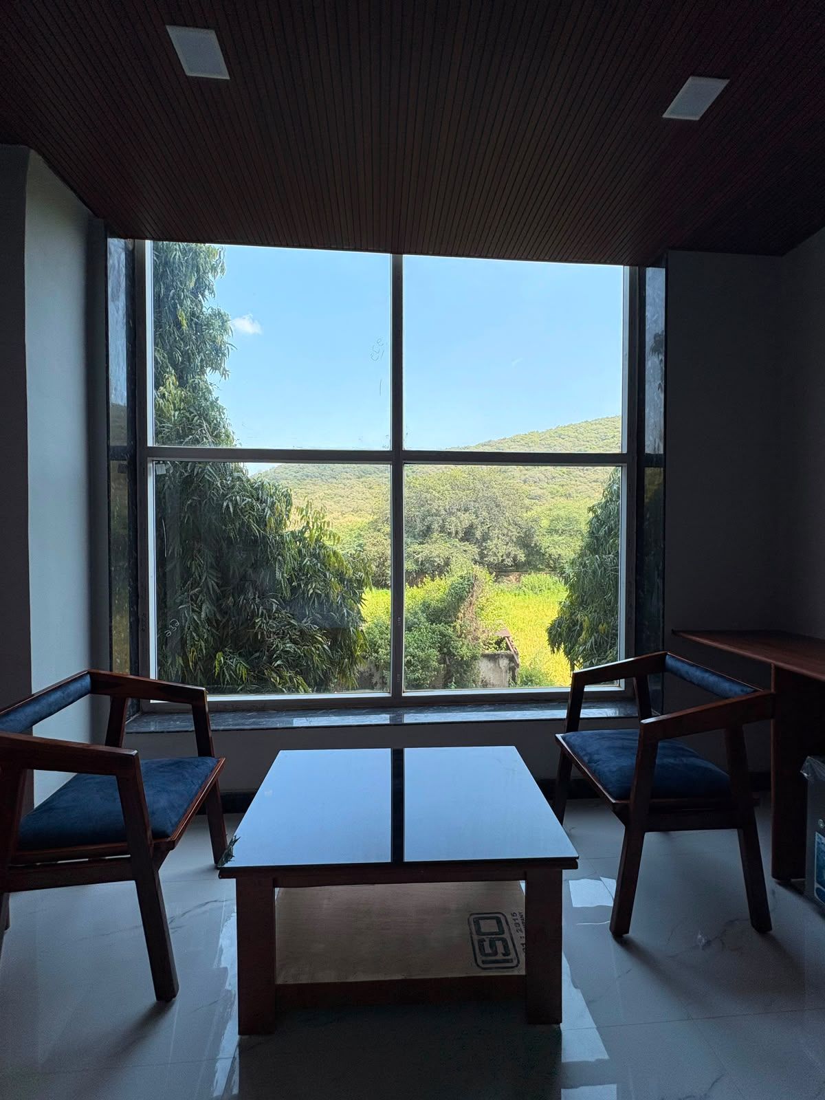 A room with a large window, two wooden chairs, a small table, and a tiled floor.