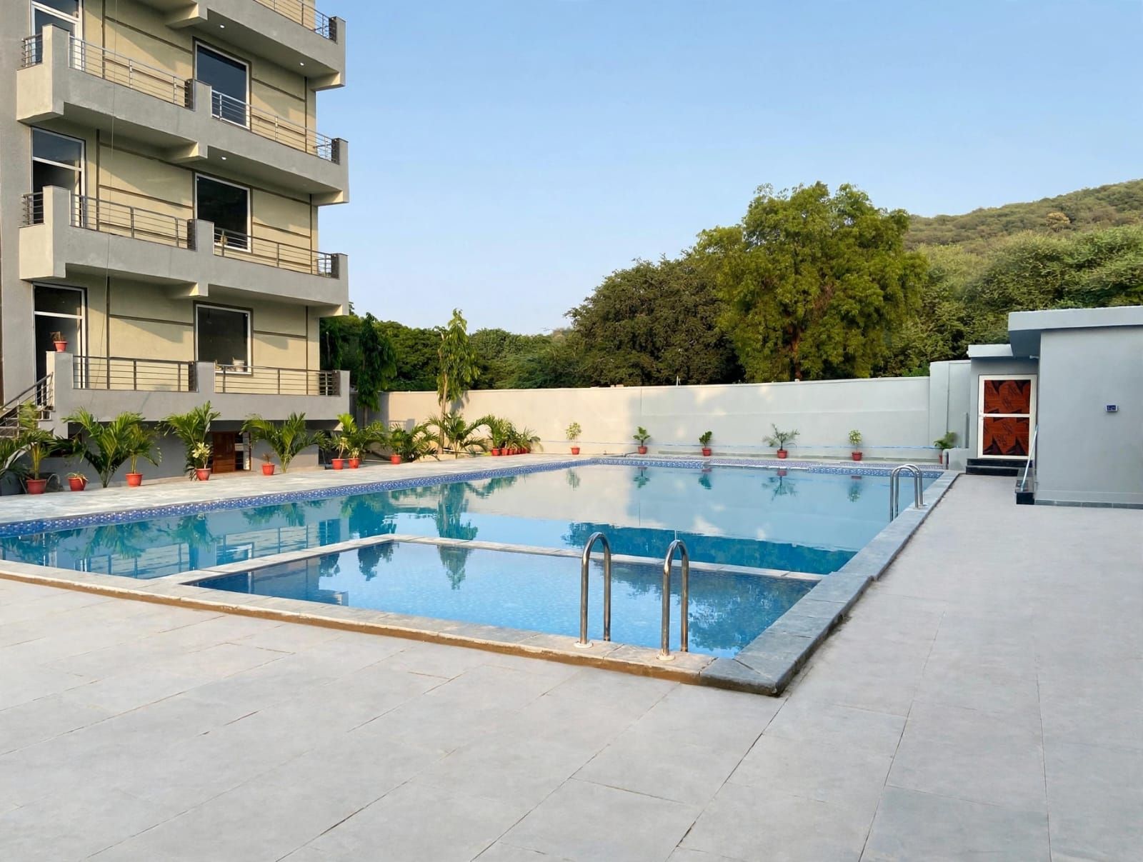 Ein rechteckiger Swimmingpool mit glasklarer, blauer Wasserfläche, umgeben von einer gefliesten Liegefläche.