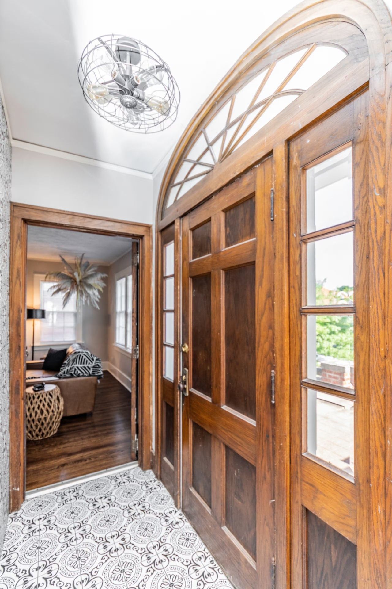 A hallway with a wooden door, a patterned floor, and a room with a sofa and decorative items.