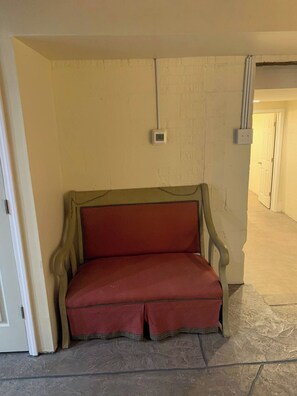 A room with a red upholstered bench against a wall, a door on the left, and a hallway leading to another room. - Chestnut Cottage at Saluda River Farms (Greenville)