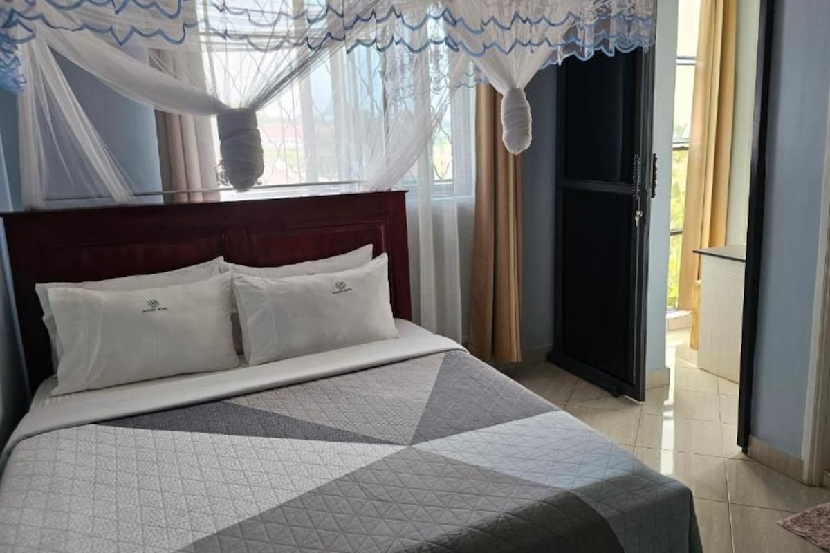Ein Schlafzimmer mit Bett, einem Fenster mit Vorhängen und einer Tür zu einem Außenbereich.