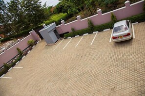 Un área de estacionamiento con un automóvil, pavimentada con baldosas hexagonales y rodeada por un muro bajo con una pequeña reja.