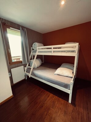 Ein Etagenbett mit Fenster und Vorhängen, Holzboden und Heizkörper.
