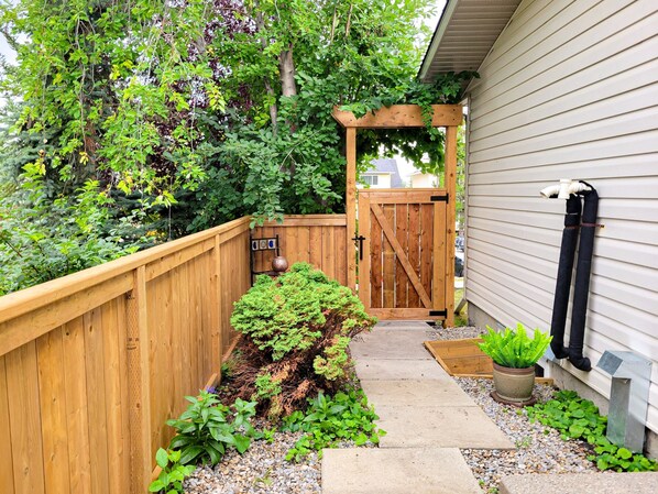 Une porte en bois mène à une maison avec un chemin de gravier et une clôture en bois.