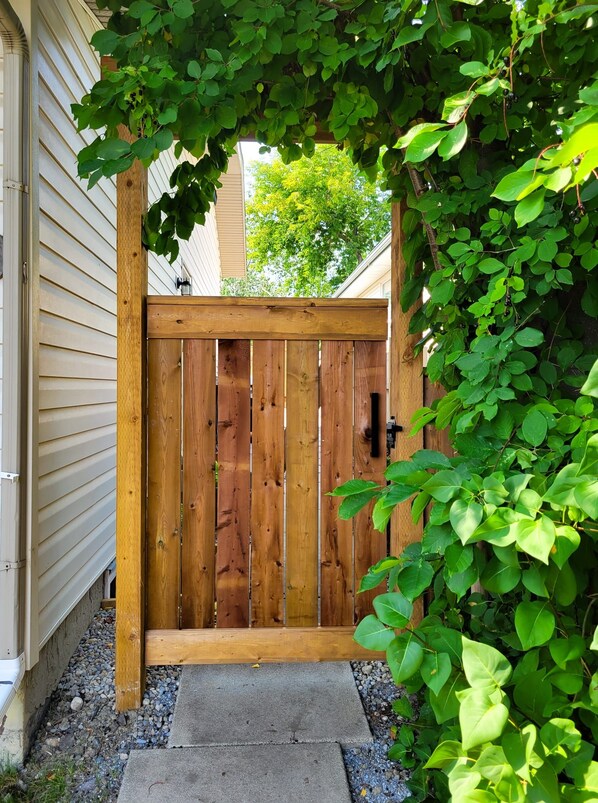 Une porte en bois avec une poignée noire, donnant sur un chemin de béton bordé de gravier et de verdure.