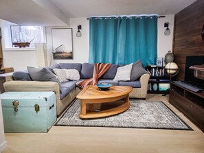 Un salon comprenant un canapé, une table basse, une valise ancienne, un globe terrestre et un téléviseur.