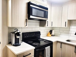 Une cuisine avec des meubles de couleur claire, une cuisinière noire, un four à micro-ondes et une machine à café.