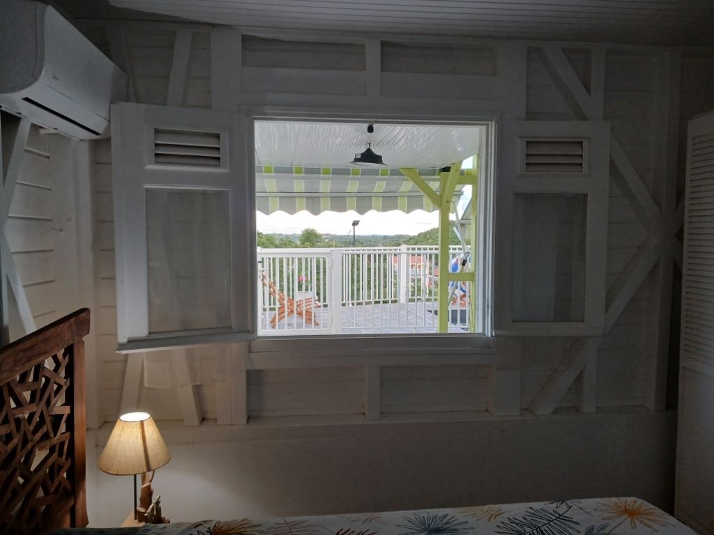A room with a window overlooking a balcony, a bed with a patterned bedspread, and a wooden headboard.