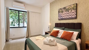 Une chambre d’hôtel comprenant un lit, une table de chevet, une lampe, une serviette, une fenêtre avec des rideaux et un tableau accroché au mur.
