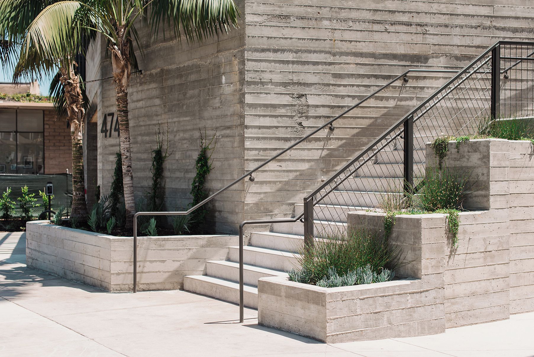 Escadaria de concreto com grades de metal, conduzindo a um edifício com fachada texturizada.