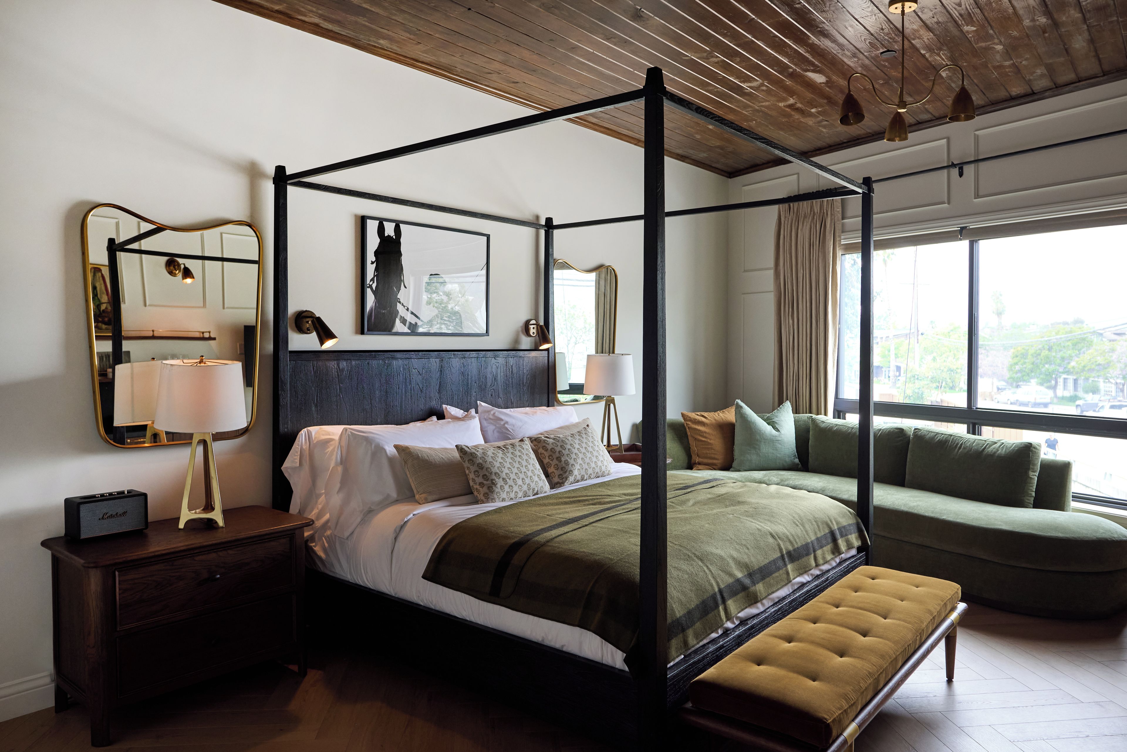 Cama de dossel com cabeceira escura, luminárias laterais e mesa de cabeceira com alto-falante.