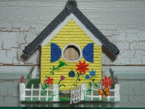 Ein Vogelhaus mit gelbem Korpus, blauen Akzenten und einem weißen Zaun an der Basis.