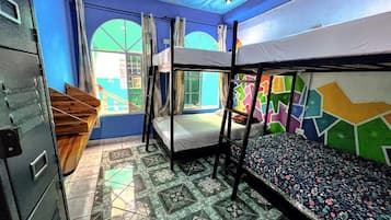 Een slaapzaal met stapelbedden, een raam met gordijnen, een betegelde vloer en een archiefkast.