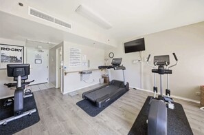 Ein Fitnessraum mit Laufbändern, einem Ergometer und einem wandmontierten Fernseher.