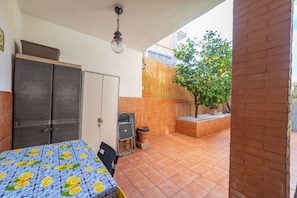 Una habitación con cama, armario, una mesita y una silla. Se ve una ventana con vistas a un árbol y un edificio.