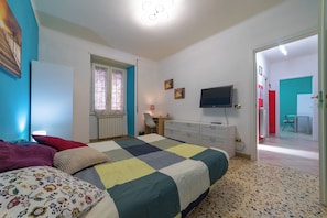 Un dormitorio con una cama, un escritorio, un televisor y una puerta que da a otra habitación.