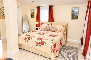 A bedroom with a floral bedspread, a bedside table with a lamp, a mirror, and a view of the outdoors through a window with curtains. - Modern DC Basement WiFi - Free Parking (Washington)